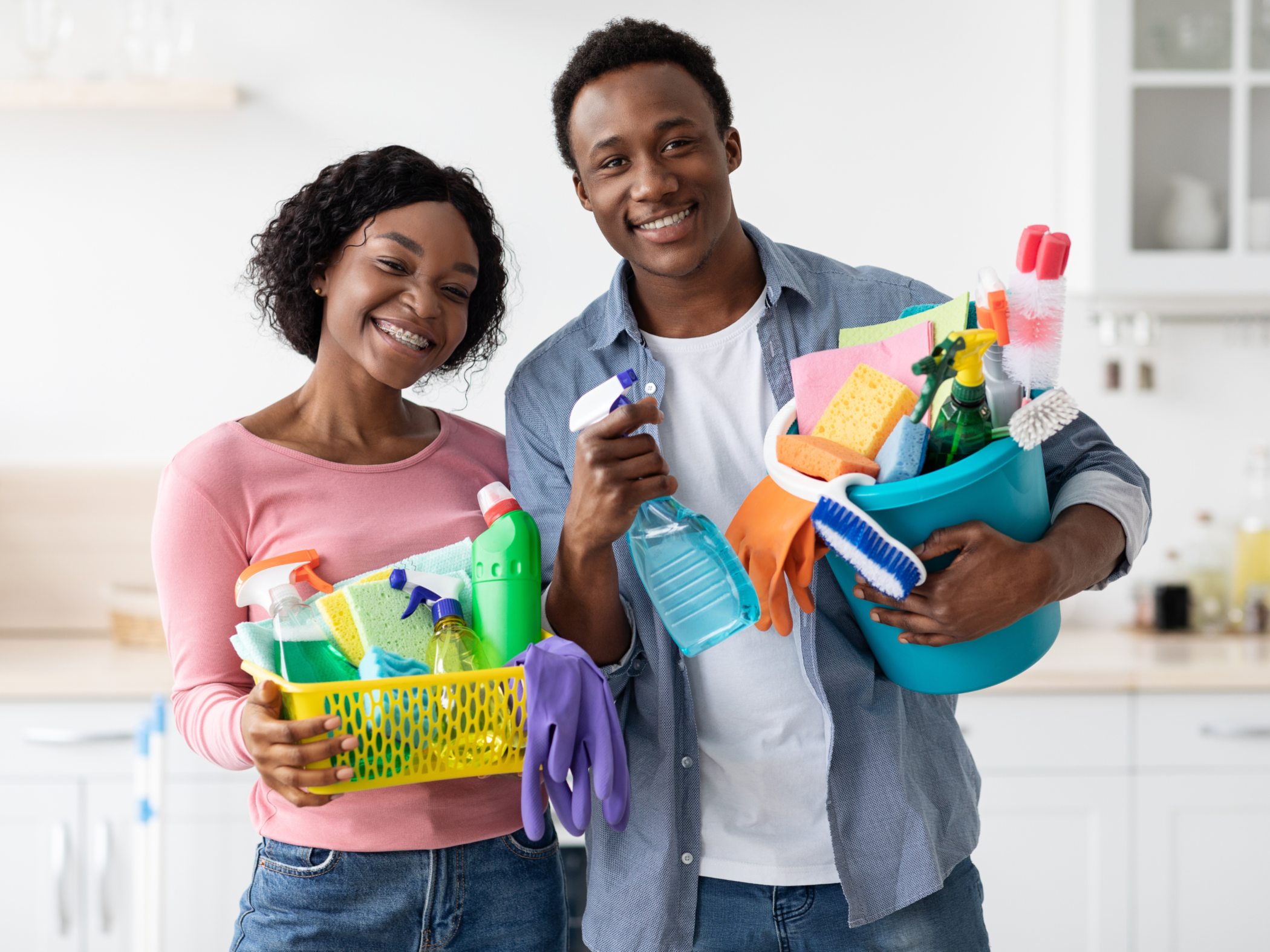 Un hombre y una mujer felices sosteniendo varios artículos de limpieza