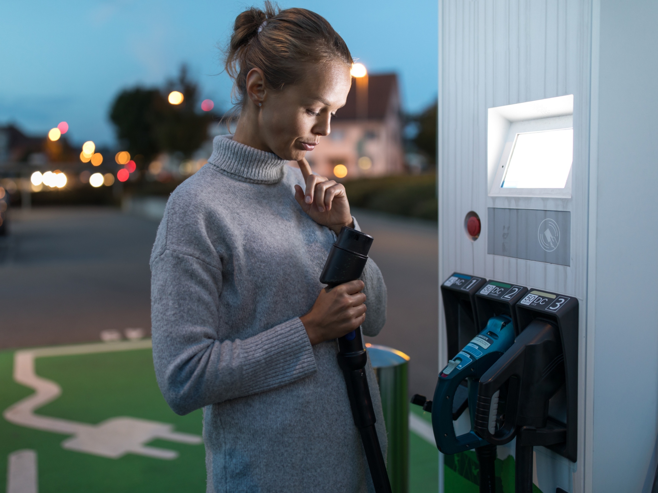 Mujer mirando un cargador de vehículo eléctrico