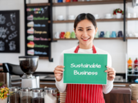 Cafe owner holding sign saying "Sustainable Business"