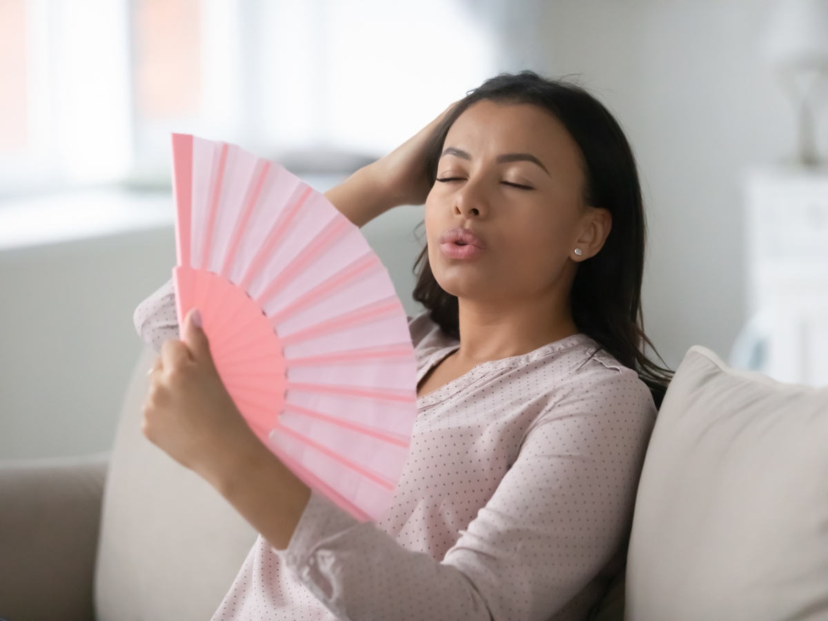 Woman sitting on a couch using a handheld fan