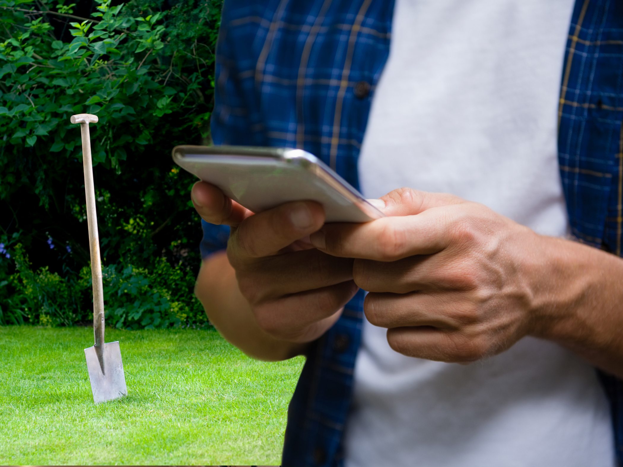 Man holding smartphone with shovel in background