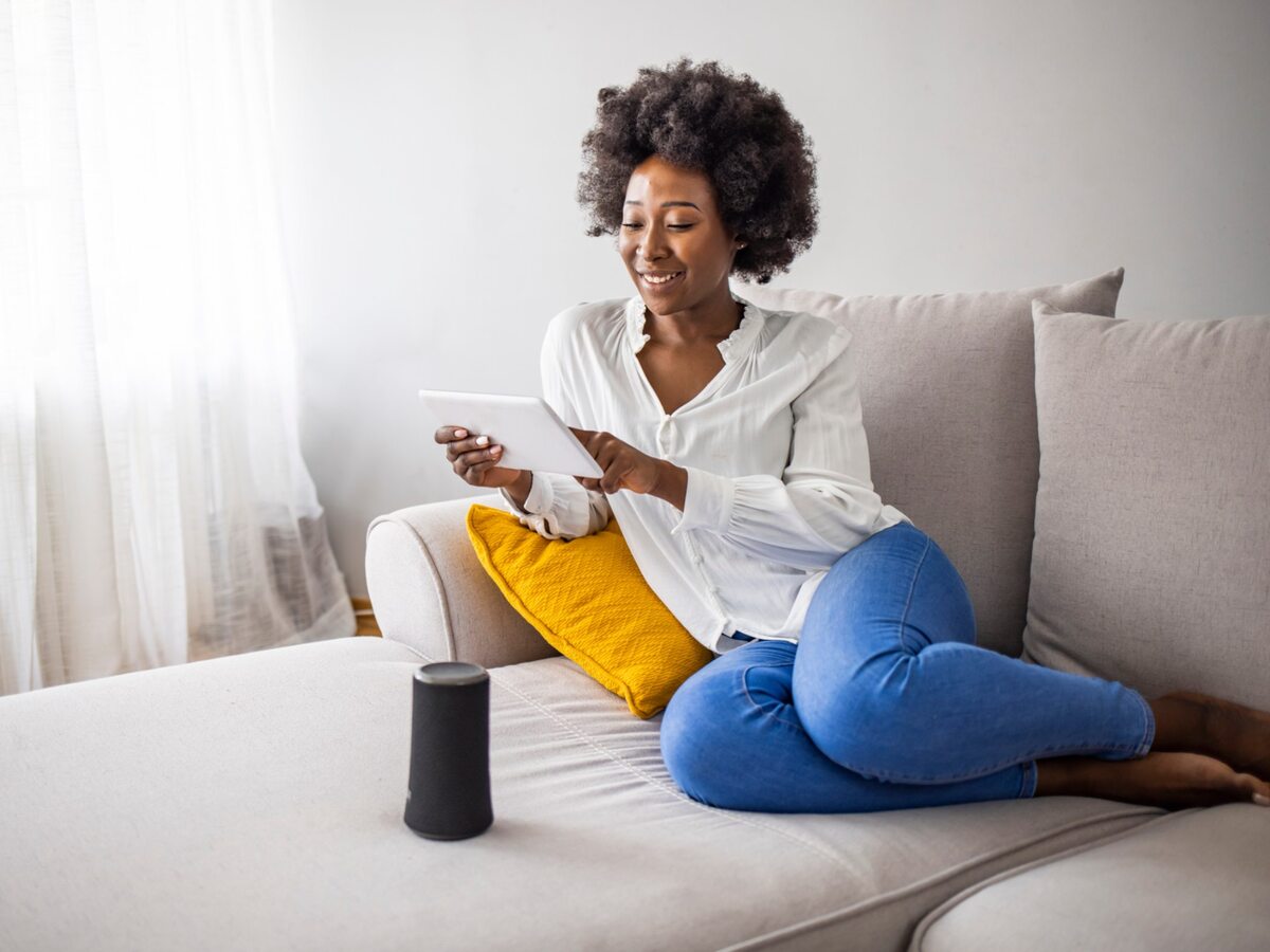 Woman on couch using computer tablet and smart speaker