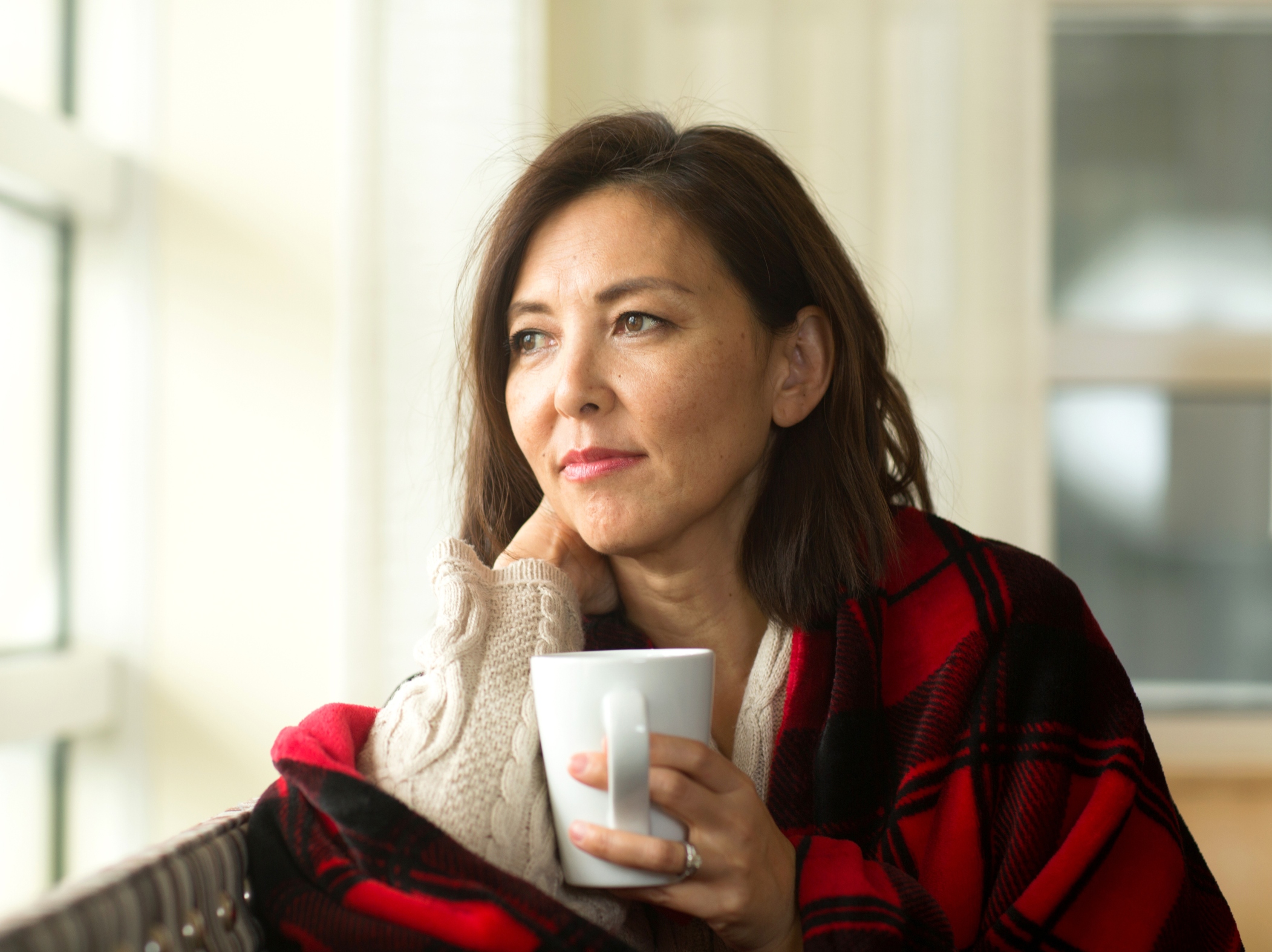 Woman sitting on couch with a blanket and cup of coffee.