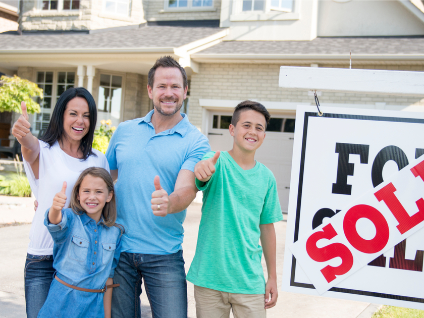 Family standing in front of house sold sign.