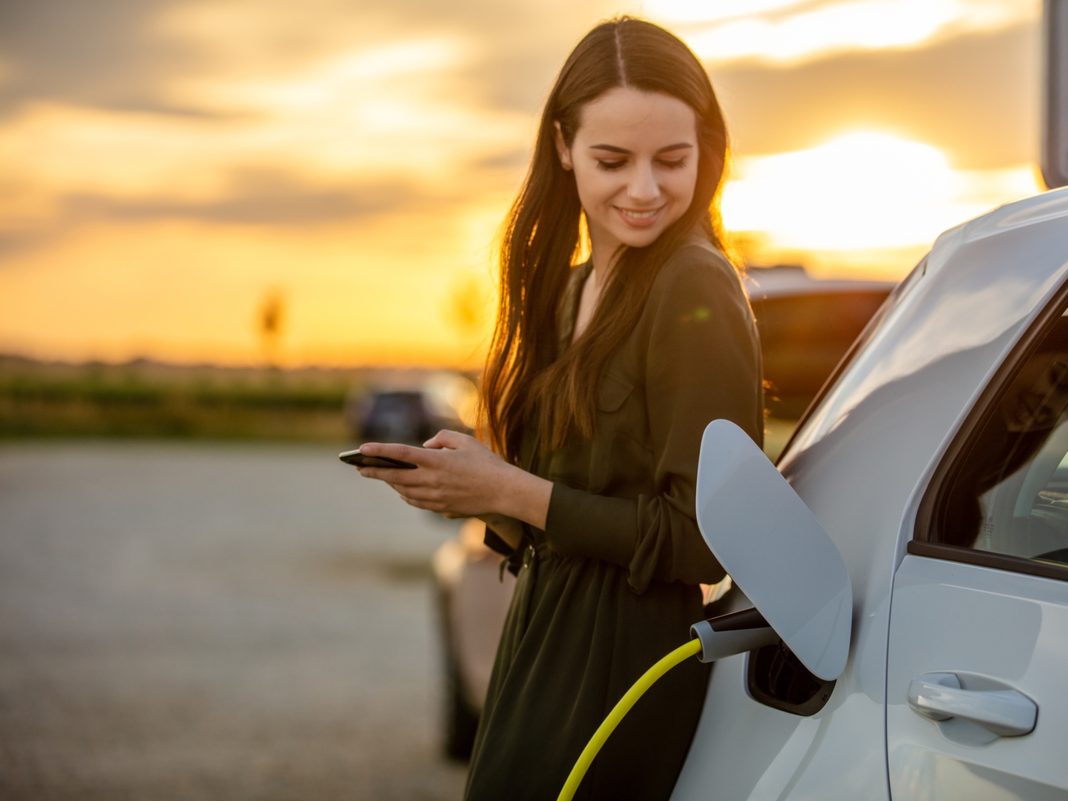 Woman holding smartphone while charging electric vehicle
